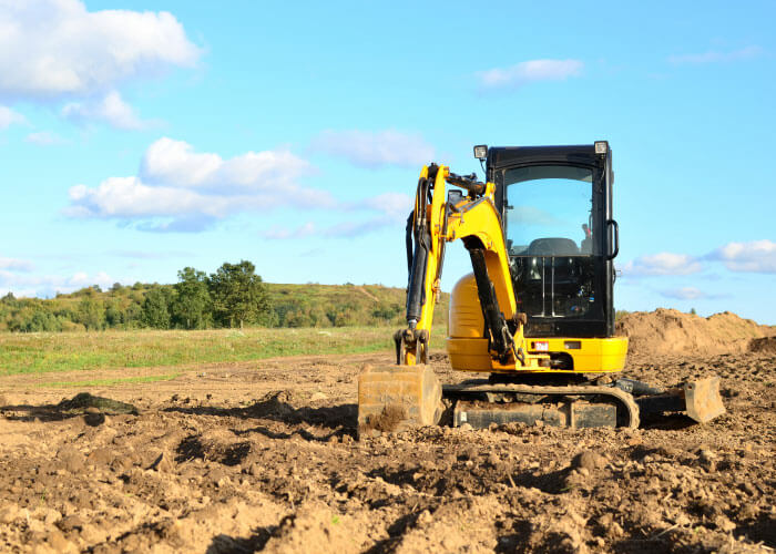 Mini excavator digging earth in a field or forest. Laying underground sewer pipes during the construction of a house.